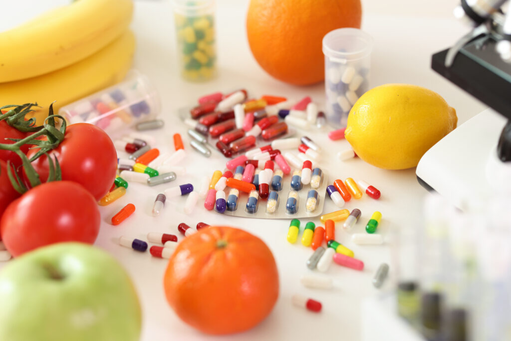 Multicolored capsules with vitamins and minerals near fresh vegetables and fruits. Food supplements lie on table with microscope and test tubes