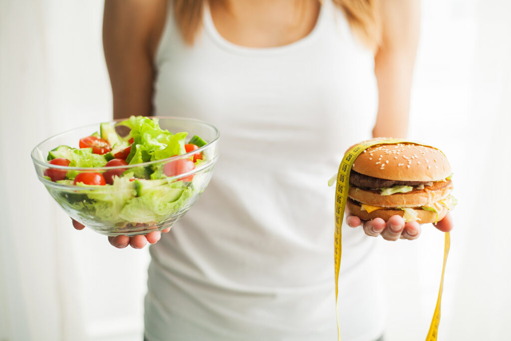 Diet. Woman Measuring Body Weight On Weighing Scale Holding Burger and Salat. Sweets Are Unhealthy Junk Food. Dieting, Healthy Eating, Lifestyle. Weight Loss. Obesity. Top View.